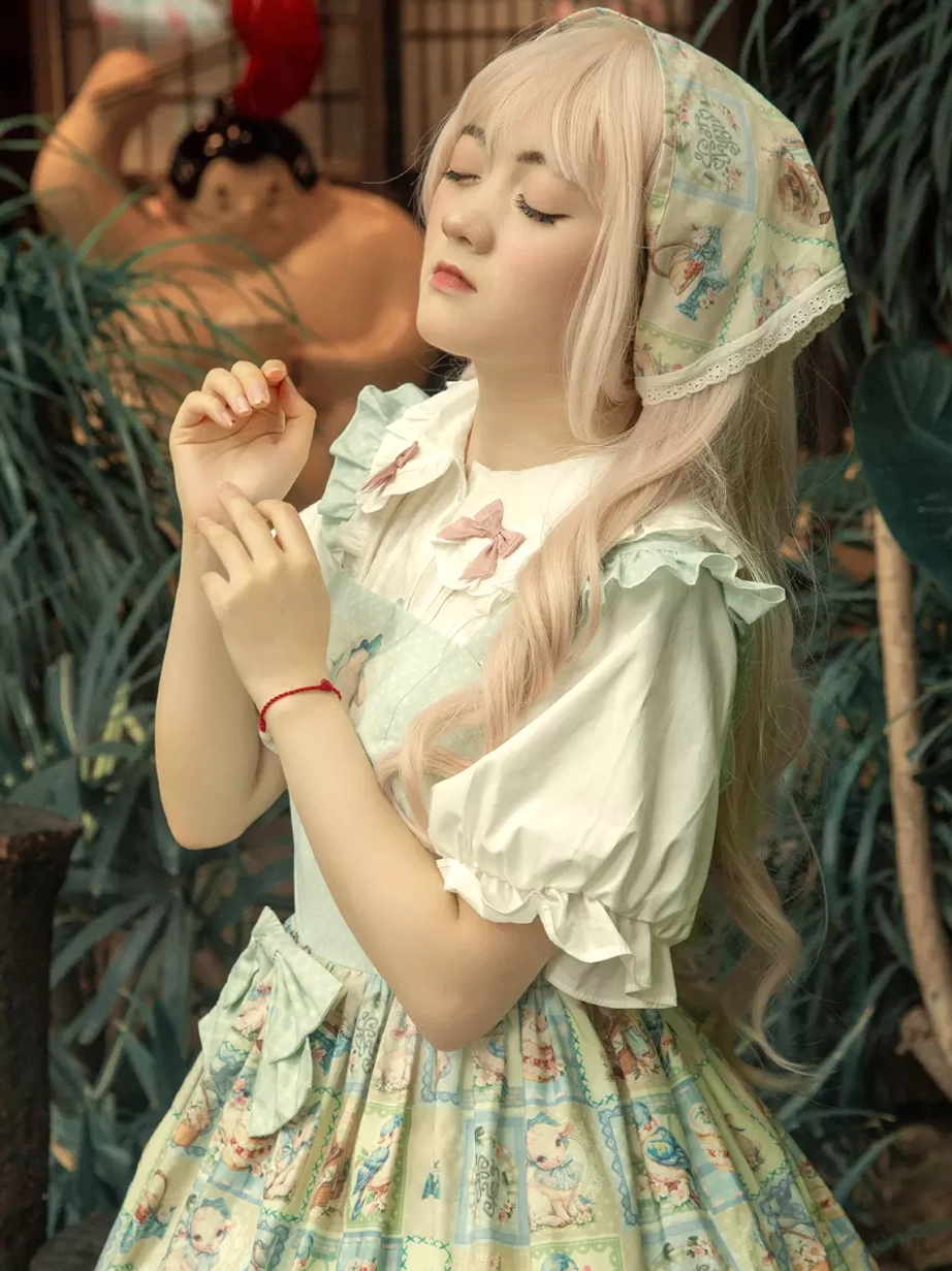 Close-up front shot of sweet lolita dress featuring matching headscarf, chest bow decoration, square print skirt pattern, gentle pose in outdoor plant setting