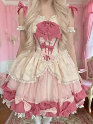 Enchanted Garden Sweet Lolita JSK Dress front full-body view with dual-tone pink fabric, oversized front bow, and layered ruffled skirt with lace accents, model wearing in pink princess bedroom setting