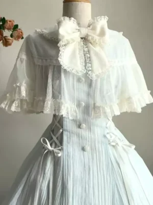 Sweet lolita dress bodice close-up showing sheer lace cape overlay, cream front bow, side lace-up closures, decorative buttons, and short sleeve details on mannequin