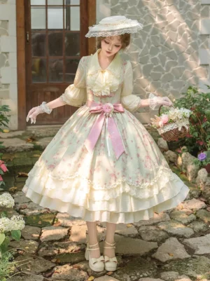 Sweet lolita JSK dress set with pale floral print and tiered ruffled skirt, worn with pink flare sleeve blouse and wide-brimmed lace hat in garden setting