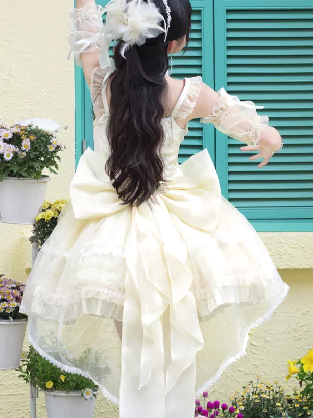 Ivory lolita JSK dress back view on model showing large back bow, high-low tulle skirt, flower hair accessory in residential outdoor scene