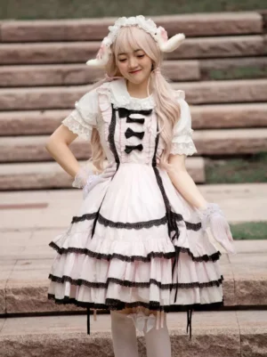 Sweet Lolita JSK sleeveless dress front view worn by model with blonde hair and sheep horn headdress on outdoor stone steps wearing pink and black tiered ruffle skirt with decorative bow