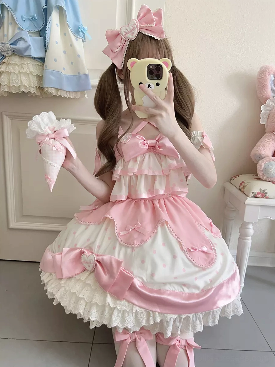 Sweet lolita jumper dress with pink and white color scheme, featuring large satin bows and layered ruffled lace hem, modeled with twin-tailed hairstyle and pink hair bow