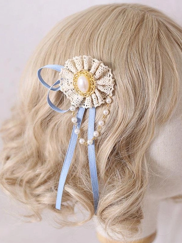 Beige lace rosette lolita hair clip with gold-trimmed pearl center, light blue ribbon accents and cascading pearl chain tassels, displayed on blonde wavy wig in lateral view