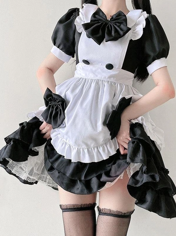 Sweet Lolita maid dress in classic black with lace-trimmed ruffled skirt, front decorative bow, matching wrist bows, and lace-top black stockings - close-up detail view