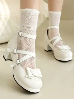 White sweet lolita mary jane pumps with heart buckles and cross ankle straps worn on model with lace socks, front side view showing bow details and round toe