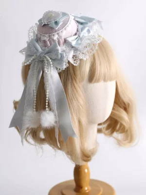 Sweet Lolita mini hat hair clip with pastel pink and light blue satin bows, delicate lace trim, and pearl pom-pom accents, displayed on blonde bob wig mannequin showcasing left rear view angle
