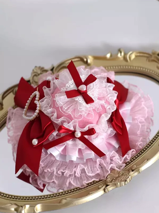 Overhead view of Sweet Lolita mini hat headdress with multi-layer frilled lace, small red ribbon bows with pearls, and heart-shaped pearl centerpiece ornament, displayed on vintage golden mirror tray showing complete design composition