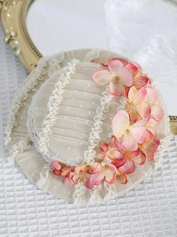 Top-down view of pink floral Lolita mini hat with beige mesh base, pink gradient hydrangea wreath, and ruffled lace trim on gold mirror