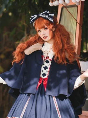Sweet Lolita navy cape with brown faux fur collar front view on model wearing red Lolita dress outdoor garden setting