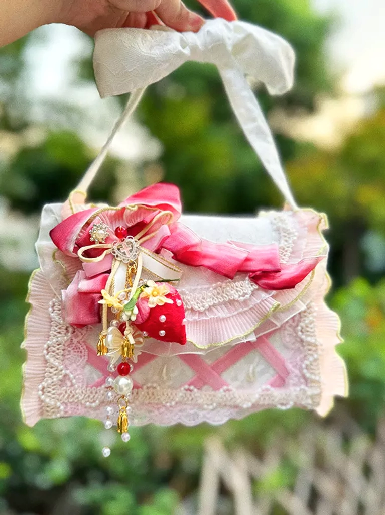 Ombre lolita handbag overhead front view with white bow shoulder strap, gradient pink ribbon bow, lace trimming, and strawberry pendant in garden setting