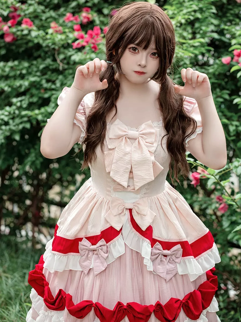 Sweet Lolita dress close-up front view with model adjusting hair, displaying front bow and double skirt bows in cream-pink-red color scheme with ruffled details