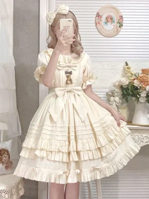Cream white sweet lolita one-piece dress with jacquard fabric, ruffled short sleeves, tiered ruffled skirt, and decorative waist bow - front view on model in vintage indoor setting
