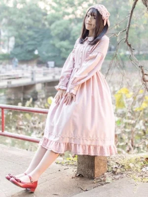 Soft pink Sweet Lolita one-piece dress with long sleeves, turndown collar, and ruffled midi hem worn by model in outdoor lakeside park setting