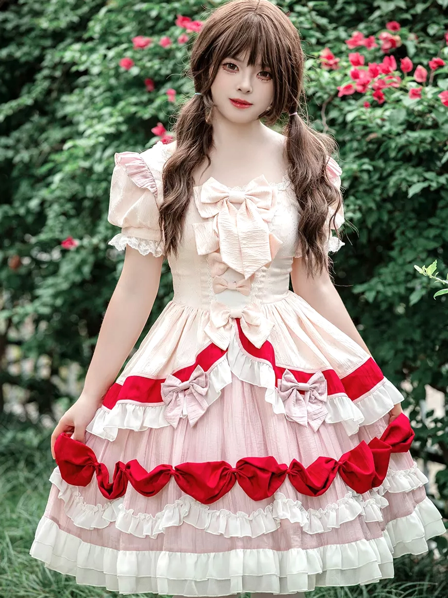 Sweet Lolita one-piece dress with square neckline and oversized front bow, featuring puff short sleeves with ruffles and multi-layered skirt with red bow trims in cream, pink and red color scheme