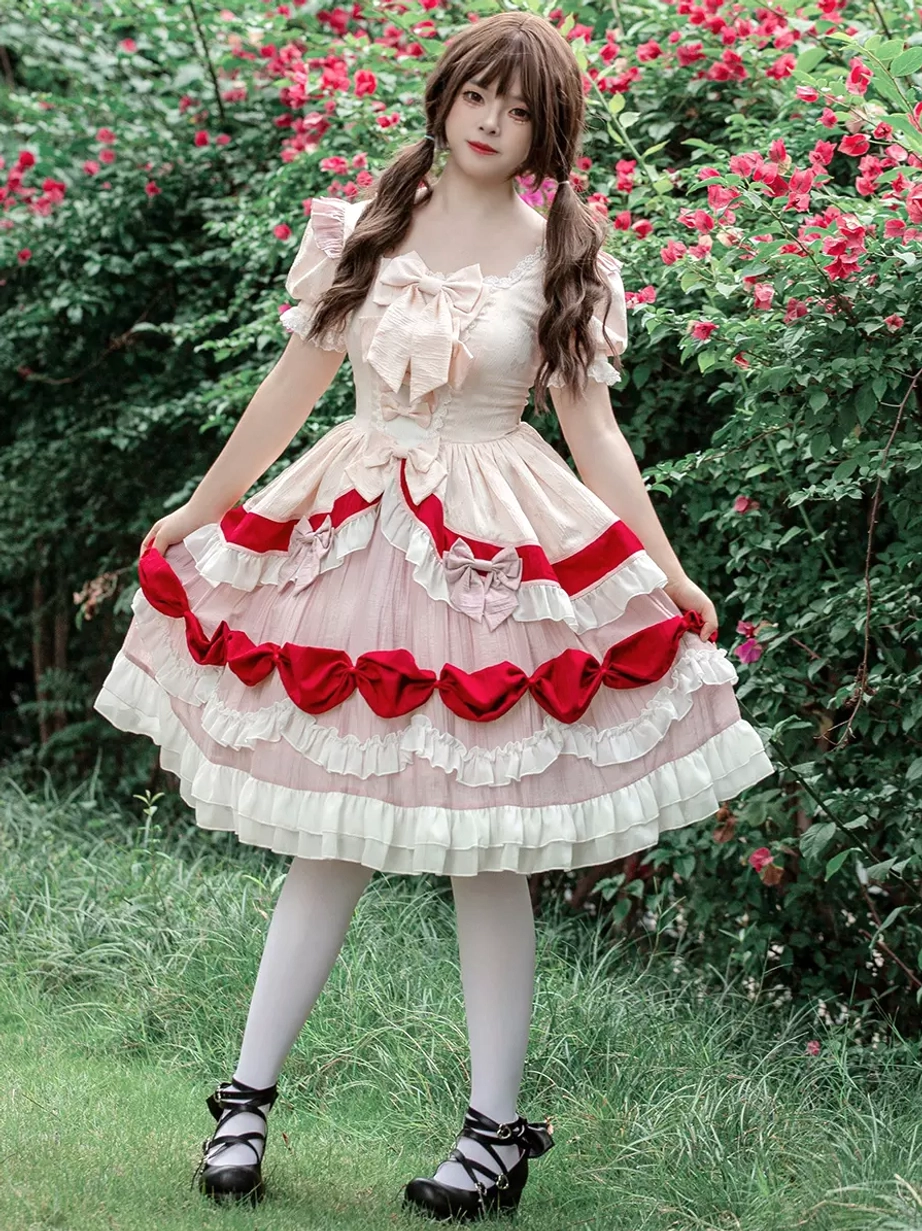 Sweet Lolita one-piece dress three-quarter front view showing cream and pink fabric with red accents, short puff sleeves with ruffled edges, and bow-trimmed layered skirt