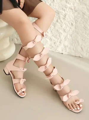 Pale pink Lolita bow sandals worn on model showing calf-high strappy gladiator design with bow embellishments, side lower leg perspective highlighting elegant strap placement
