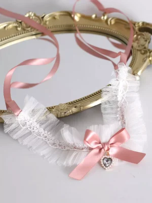 Sweet Lolita pink heart choker necklace with pearl-trimmed gem pendant and white ruffled mesh lace trim, featuring delicate pink satin bow detail on vintage ornate gold mirror tray