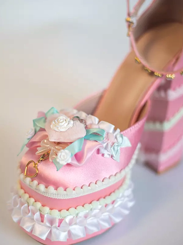 Sweet Lolita pumps close-up top front view displaying pink satin upper with elaborate floral and bow front decoration, thick ruffled sole edge detail