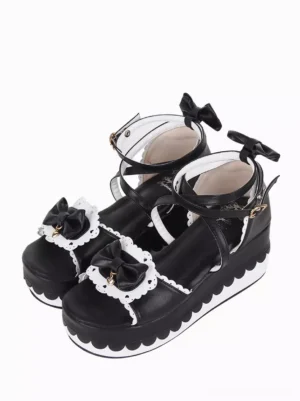 Sweet Lolita black and white platform sandals front three-quarter view showing scalloped sole edge, lace-trimmed bow toe cap, and wedge heel design on white background