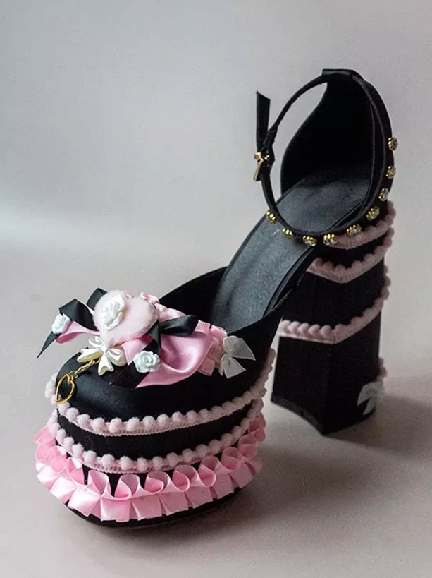 Black-pink themed Sweet Lolita platform pumps front three-quarter view with black upper, pink ruffled trims, floral and bow ornament, chunky heel base
