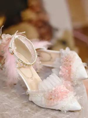 Sweet lolita high heel pumps side close view featuring pointed toe, ruffled trim, pink floral decorations and pearl ankle chain on lace tabletop setting