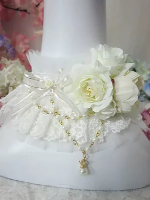 Rococo sweet lolita white choker with ruffled lace collar, artificial ivory roses, satin bow, and gold pearl pendant on neck mannequin with floral backdrop