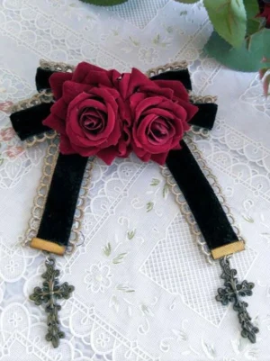 Sweet lolita rose cross brooch with black velvet bow, wine red artificial roses, and vintage gold cross charms on embroidered lace tablecloth flat lay