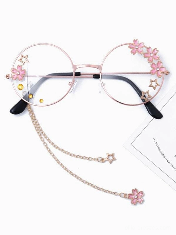 Sweet lolita round frame glasses with dual chain charms, pink flower pendants, star decorations, rose gold frame with yellow dot lens details, top-down front view with paper card prop