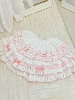 White Sweet Lolita skirt with pink tiered ruffles small pink bows and elastic waistband flat lay overhead view wooden floor