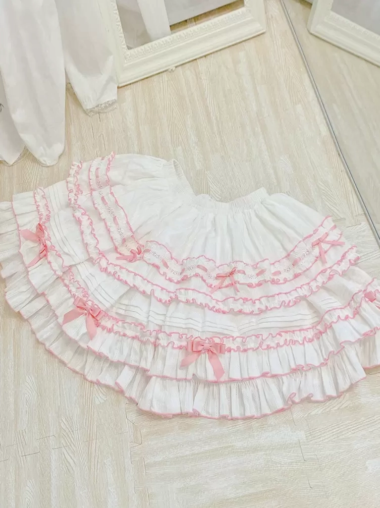 White Sweet Lolita skirt with pink tiered ruffles small pink bows and elastic waistband flat lay overhead view wooden floor