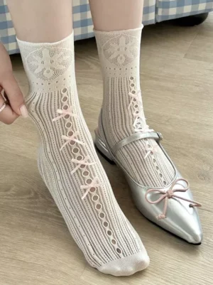 Sweet lolita mid-calf socks with pink bow accents shown on model wearing silver ballet flats, hollow knit cream white texture close-up foot view