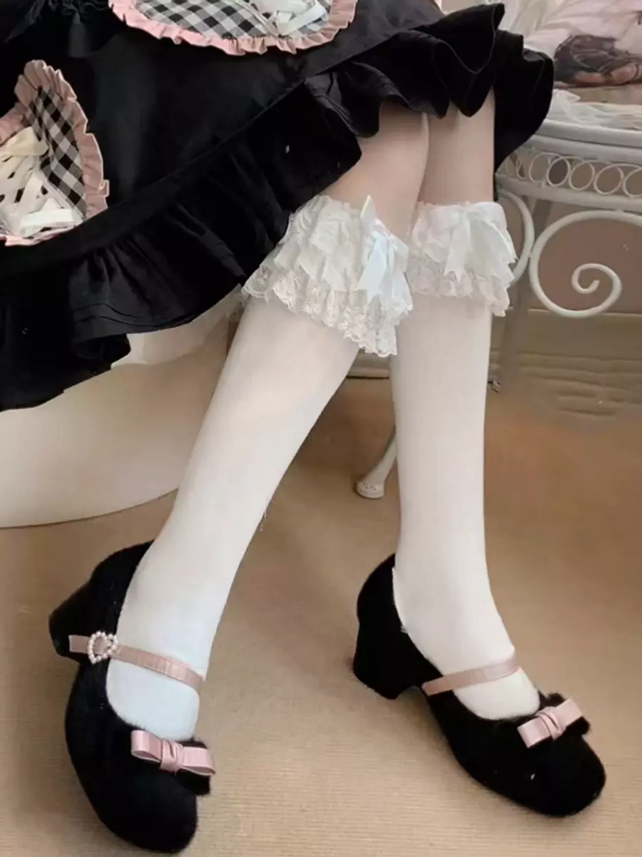 Side low-angle view of sweet lolita socks with white sock body and frilled white lace trim without extra bow, styled with black Mary Jane shoes with pink bow details on chair