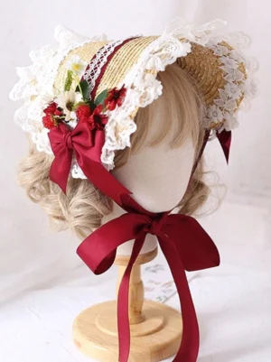 Sweet Lolita straw bonnet headdress with beige woven straw, white ruffled lace trim, red satin bow, red flowers and berries, long red chin straps, displayed on blonde curly wig mannequin three-quarter front view