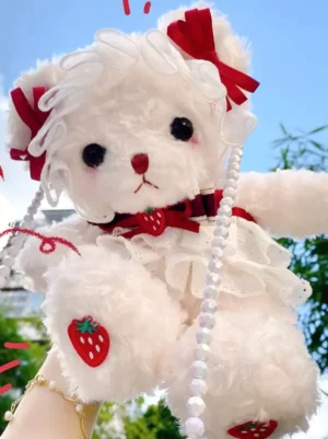 Sweet Lolita plush bear crossbody bag in white with red strawberry bows, held on wrist with gold bracelet, outdoor setting, pearl shoulder strap detail, strawberry paw patches
