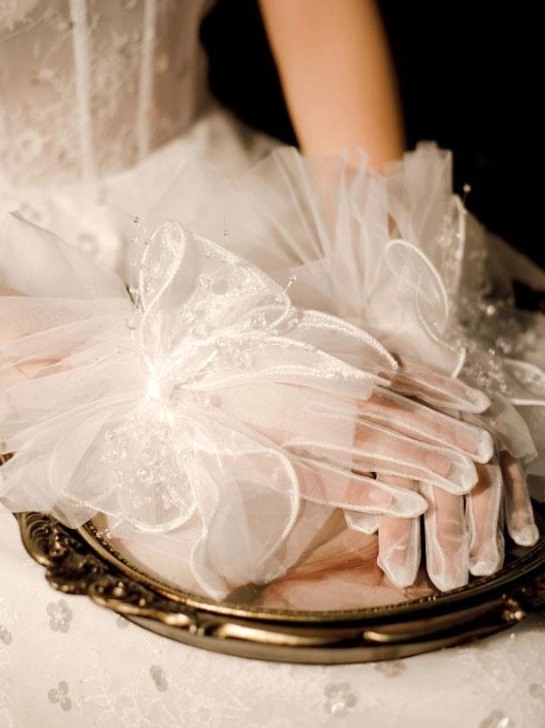 white mesh bow gloves with big bow design and semi-transparent tulle fabric displayed on vintage carved metal tray with lace tablecloth and wedding dress top-down view