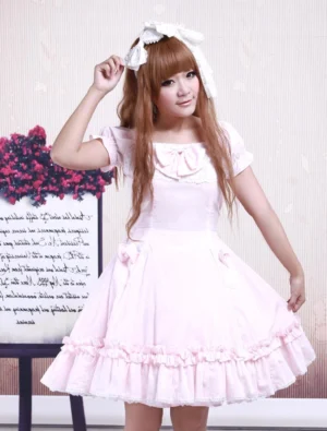 Sweet pink cotton lolita dress front three-quarter view worn by model with white hair bow and brown hair, featuring ruffled skirt hem and chest bow decoration, square neckline