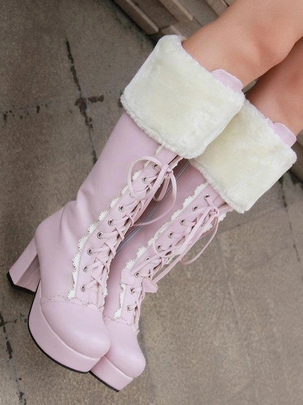 Sweet pink lolita boots worn on model's feet low side view on concrete background, showcasing white fluffy cuff, lace-up front, platform block heel in styled wear
