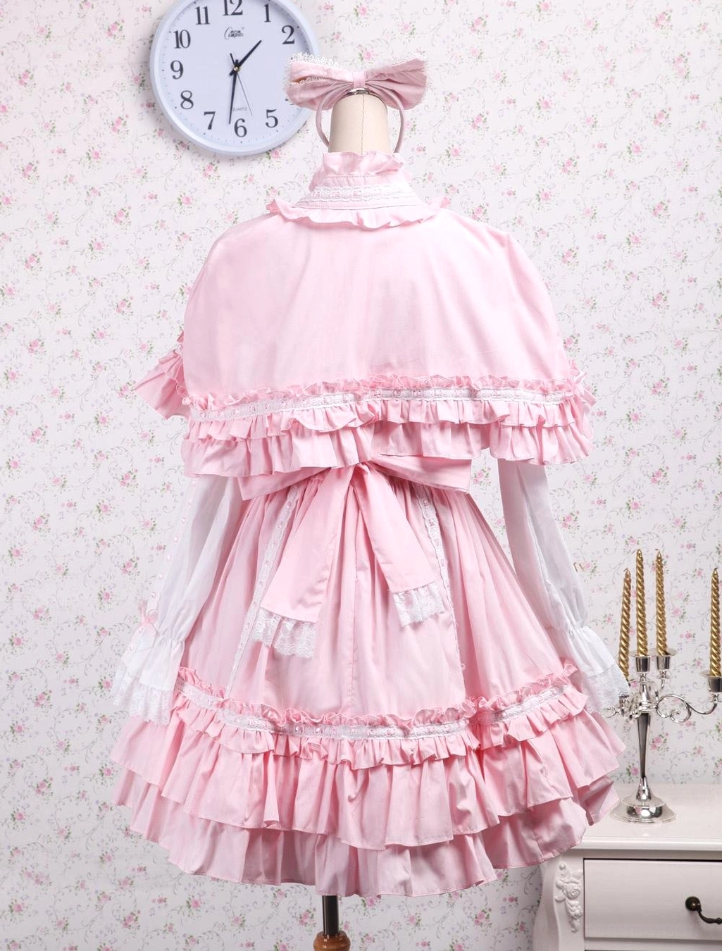 Back view of sweet pink lolita cape dress set on dress form showing ruffled capelet with lace trim bow sash tiered ruffled skirt hem