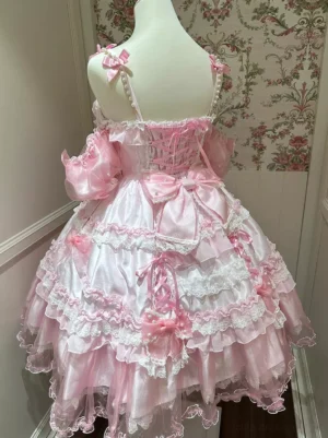 Pink sweet lolita dress back view featuring lace-up corset back, layered ruffle tulle skirt, and oversized bow with pearl chain details