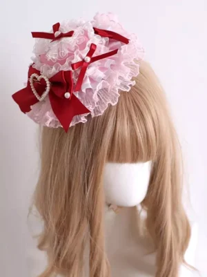 Sweet Rococo pink lace lolita mini hat headdress with red satin bows and pearl heart ornament front three-quarter view on mannequin with light brown wig