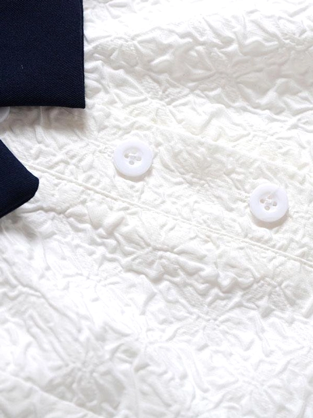 Close-up flat lay detail shot of sweet sailor lolita dress showing embossed white textile fabric round white buttons and navy fabric swatch colors