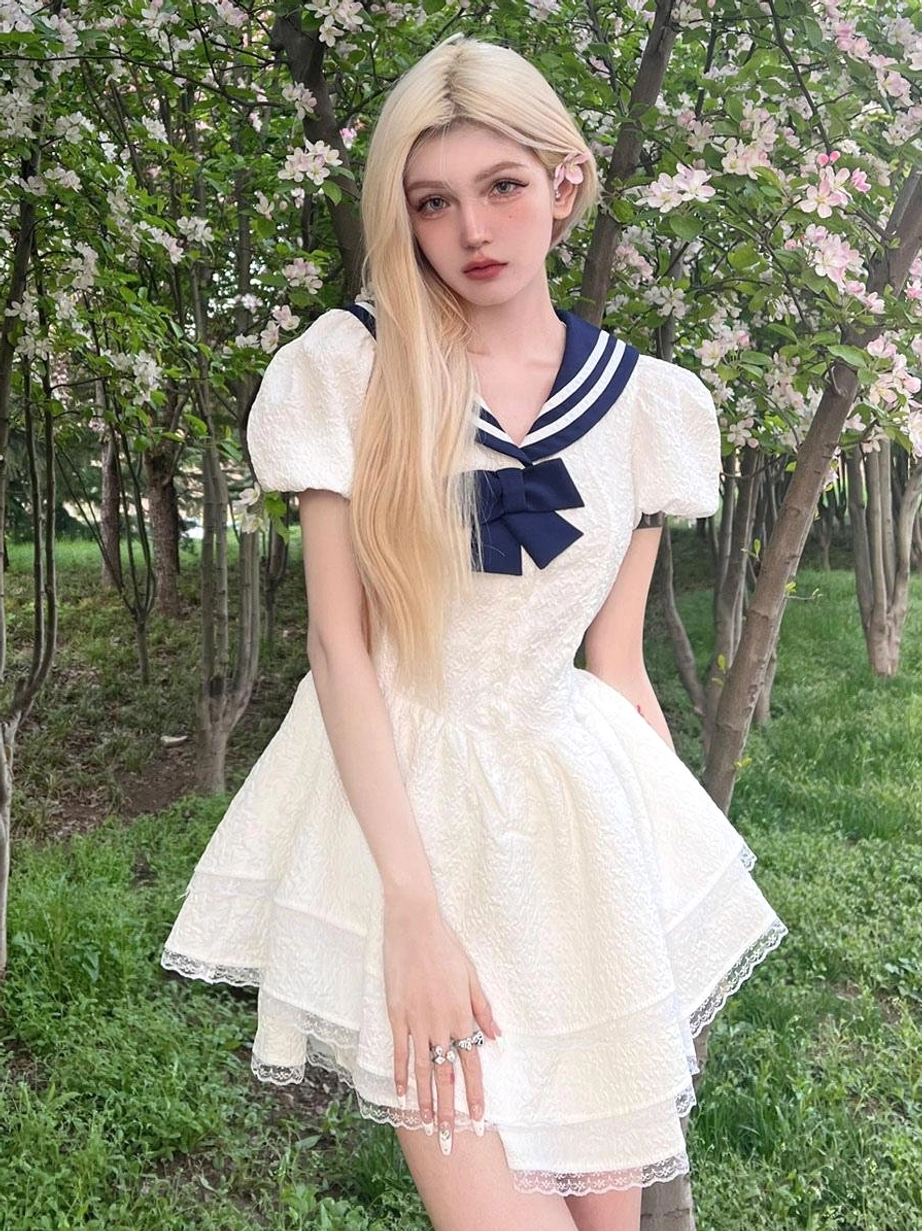 Full body outdoor portrait of blonde model wearing sweet sailor lolita mini dress with navy sailor collar white layered ruffles and puff sleeves in flower garden setting