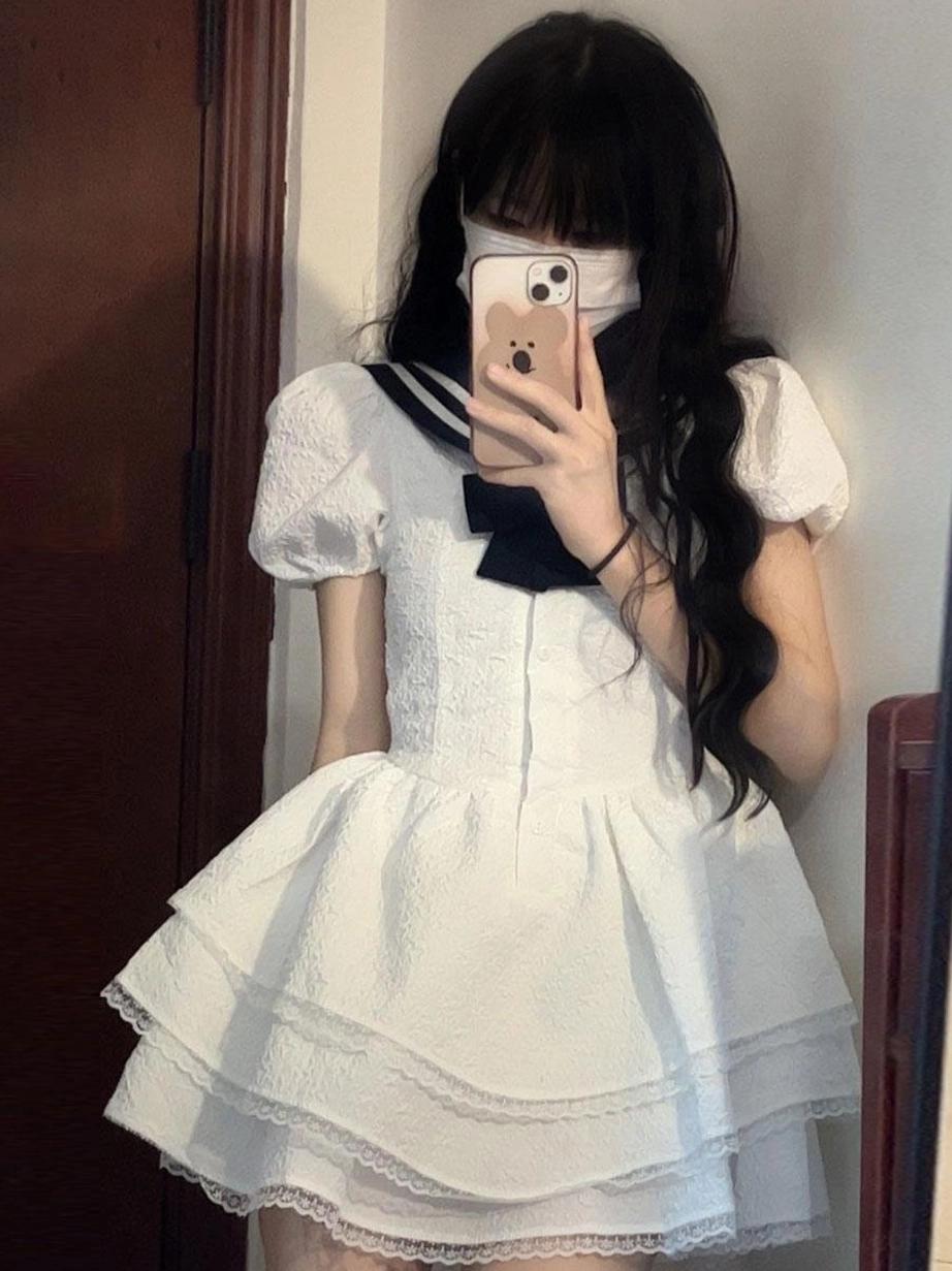 Mirror selfie front view of dark-haired model wearing sweet sailor lolita dress with black bow navy sailor collar puff sleeves and lace-trimmed ruffle skirt