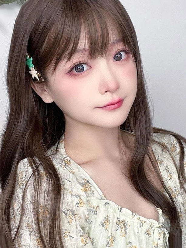 Close-up portrait view of tan-brown lolita wig with air bangs and star-shaped hair clip, worn by female model in floral blouse, showcasing realistic hair texture and styling details