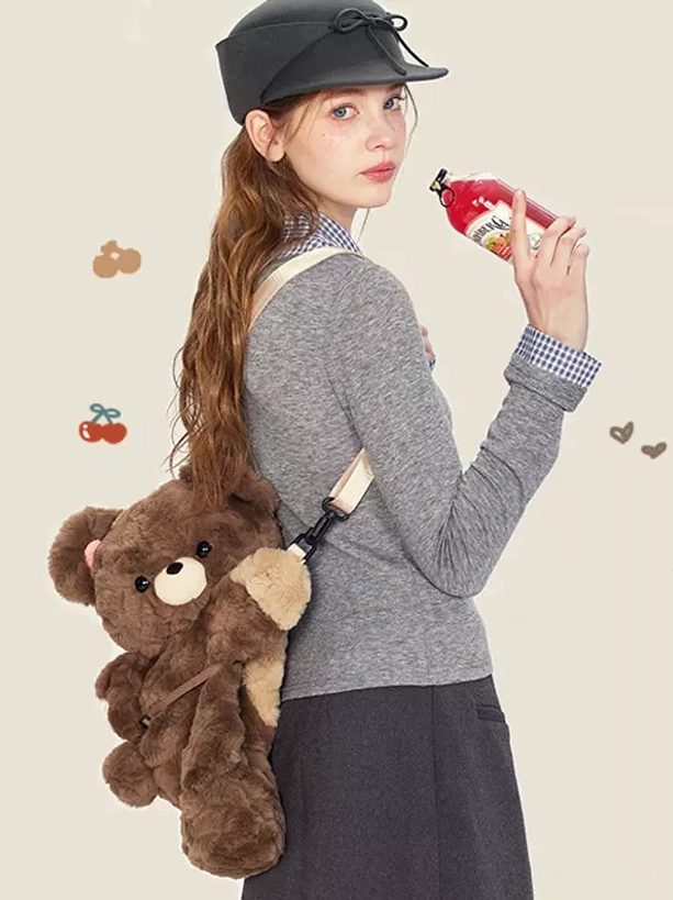Brown teddy bear plush lolita crossbody bag worn on model's shoulder with beige strap and light brown paws visible, styled with gray knit top and black accessory hat