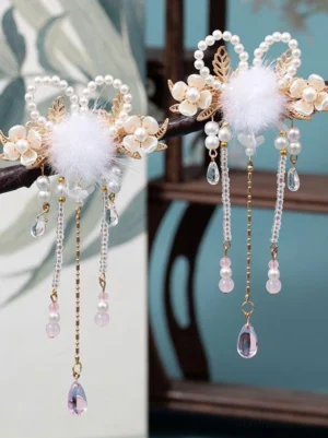East Asian inspired decorative hair clips featuring gold metal, soft white pom-poms, dangling pearl-adorned tassels with pink purple pendants, wooden furniture display