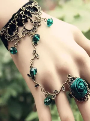 Vintage lolita hand chain worn on real hand with green plant background showing faceted emerald rhinestone pendants and satin rose ring