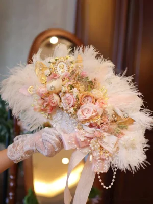 Vintage wedding hand flower bouquet with blush pink blooms, gold trims, and satin ribbon, held by gloved hand with mirror background reflection - classic lolita bridal prop