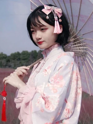Young girl wearing pink sakura wa lolita hair headdress with bell charms styled with floral traditional kimono outfit outdoors with paper umbrella
